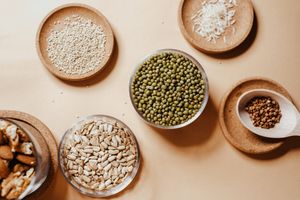 Flat lay of assorted seeds and nuts in rustic saucers on a neutral background, showcasing natural textures.